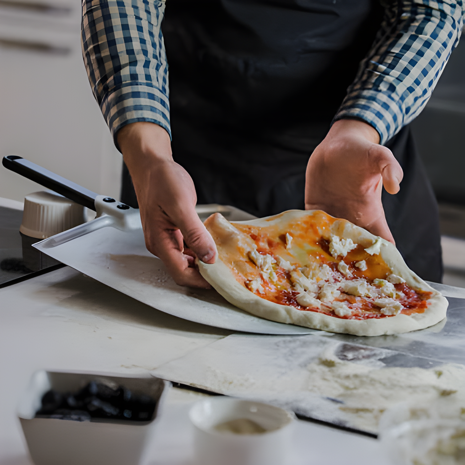 Person preparing a pizza on a kitchen counter