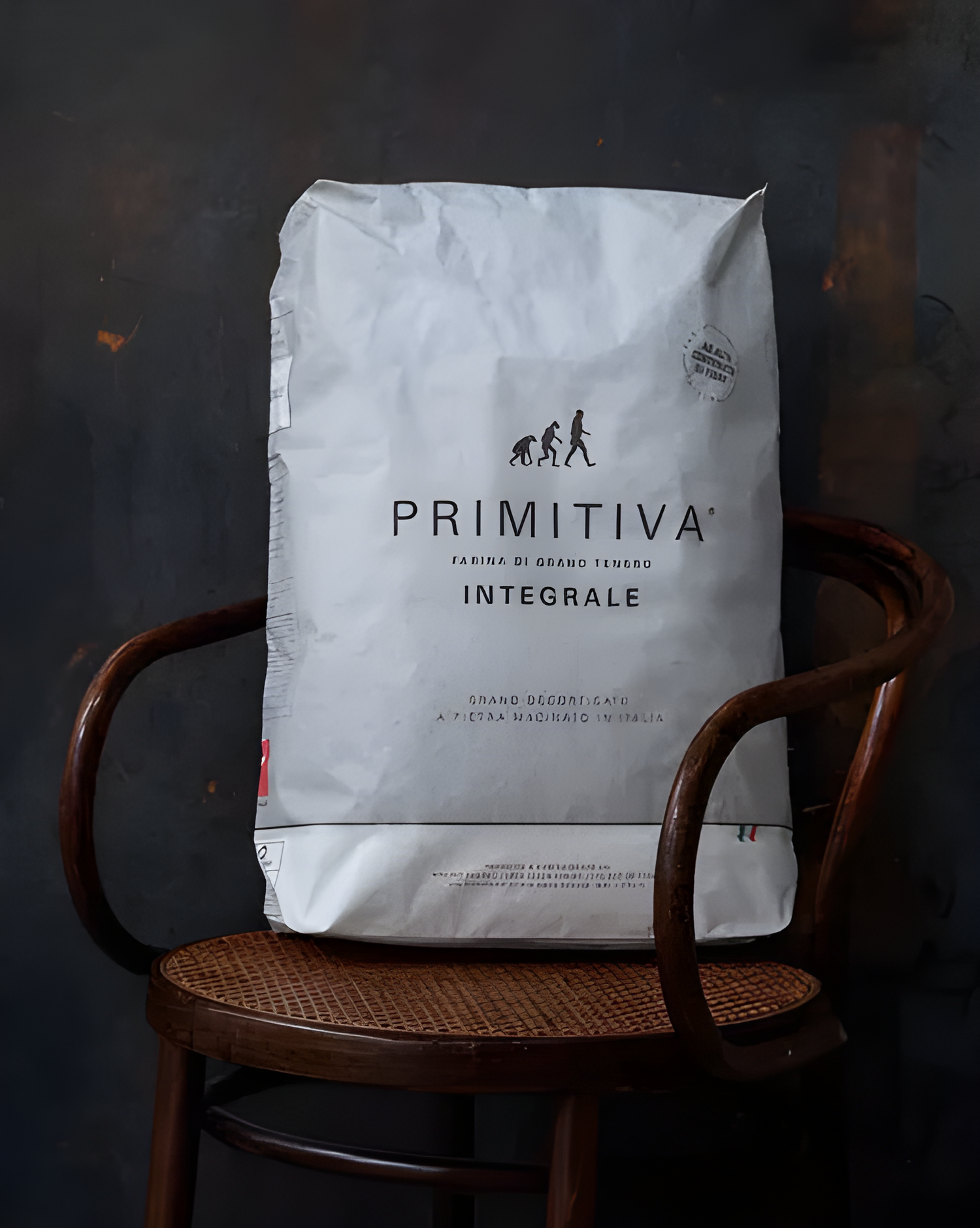 Primitiva flour bag on a wooden chair against a dark background