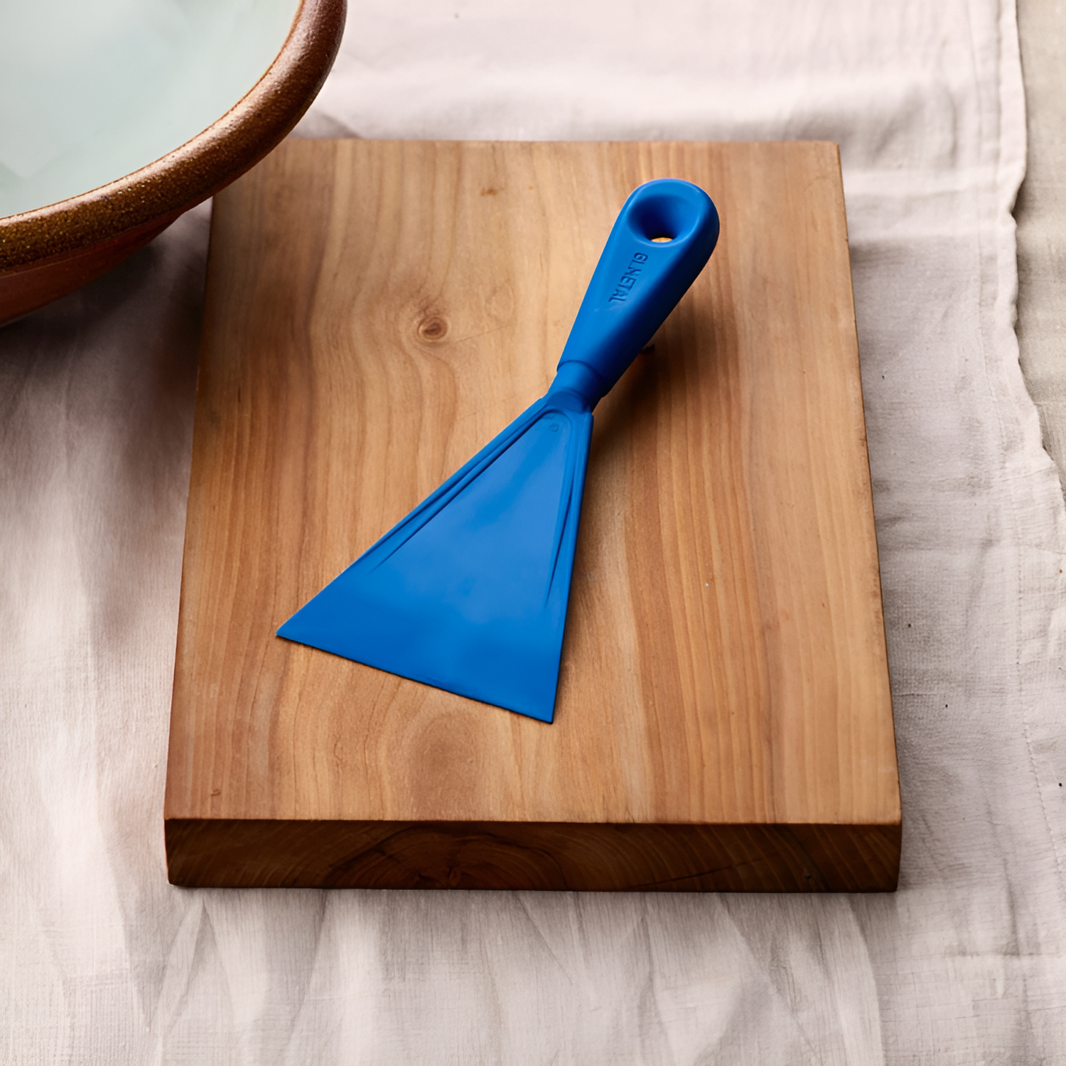 Blue scraper on a wooden cutting board with a white towel in the background