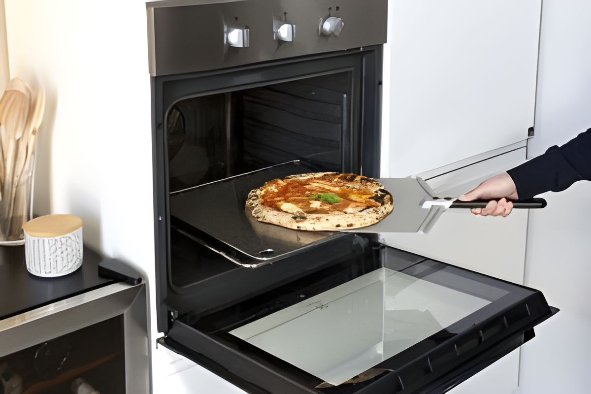 Person taking a pizza out of an open oven using a spatula.
