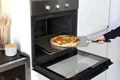 Person taking a pizza out of an open oven using a spatula.
